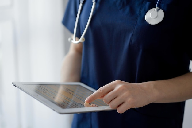 Foto mulher médica usando um tablet enquanto está perto de uma janela panorâmica na clínica de perto médico ou cirurgião no trabalho conceito de medicina