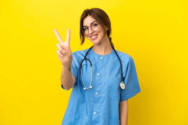 Mulher médico cirurgião isolada em fundo amarelo sorrindo e mostrando sinal de vitória