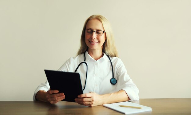 Mulher médico com documentos de estetoscópio computador tablet digital sentado na mesa no escritório da clínica