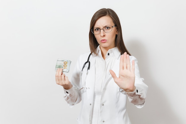 Mulher médico mostrando gesto de parada com a palma da mão isolada no fundo branco. Médica em vestido de médico com estetoscópio segurando notas de dinheiro, maço de dólares. Conceito de pessoal de saúde.