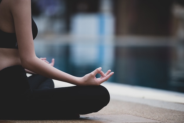 Mulher meditando ao lado da piscina.