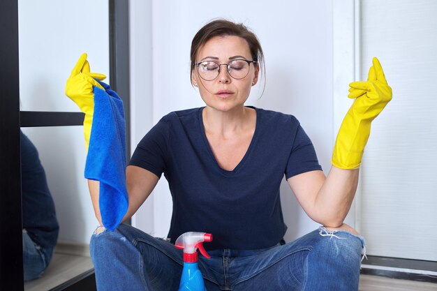 Mulher meditando cansada triste em luvas com detergente e pano, sentada no chão na sala terminou de limpar a casa. higiene, pureza, casa, conceito de limpeza