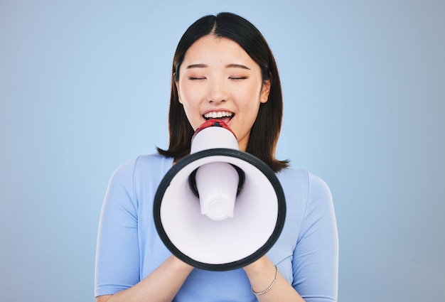 Mulher megafone e voz para transmissão de notícias ou venda de estudantes e anúncio em fundo azul Jovem asiático com ruído para chamada à ação atenção universitária ou palestrante universitário em estúdio