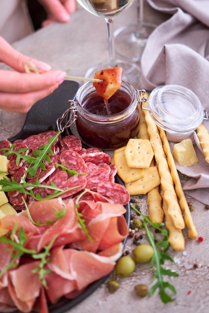 Mulher mergulha queijo parmesão em molho Dois copos de vinho branco e prato de carne antepasto italiano