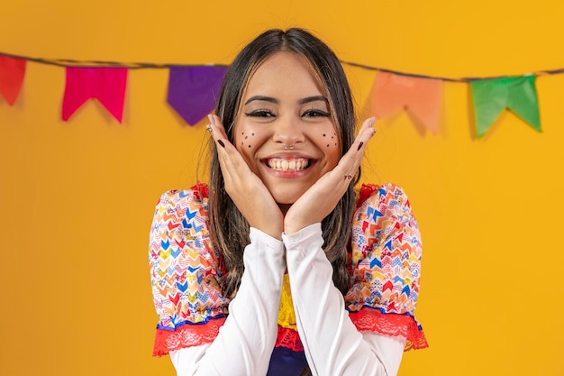 Mulher mestiça com traços asiáticos vestindo roupas típicas para a festa junina com bandeiras coloridas ao fundo