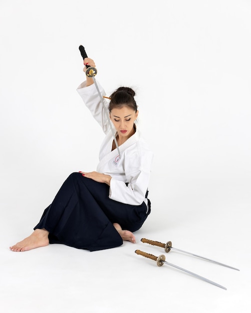 Mulher mestre de Aikido no quimono tradicional samurai hakama com faixa preta com espada katana no fundo branco Estilo de vida saudável e conceito de esportes