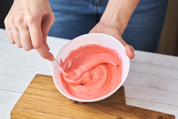 Mulher mexendo creme vermelho para decorar biscoitos em uma tigela na cozinha, closeup