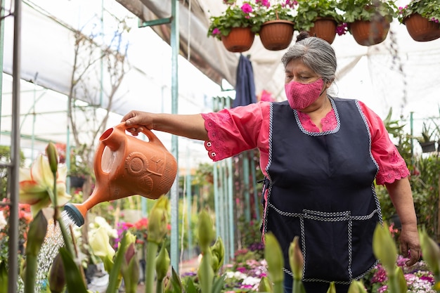 Mulher mexicana regando plantas no viveiro de Xochimilco, México, usando máscara facial, novo normal