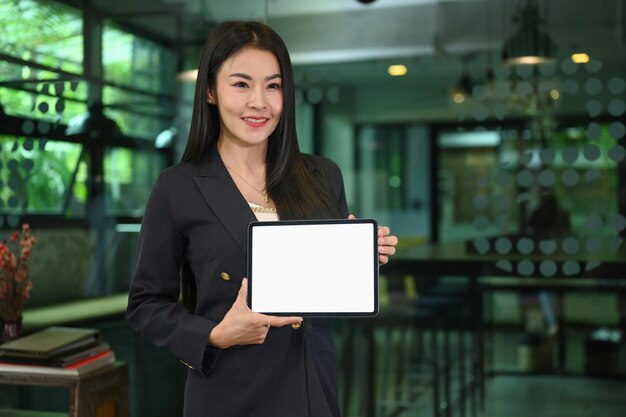 Mulher milenar confiante em terno de negócios segurando a tela vazia do tablet digital para o seu texto de anúncio