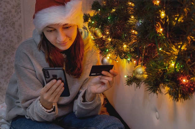 Mulher milenar faz compras de Natal on-line segurando um telefone celular e um cartão de crédito