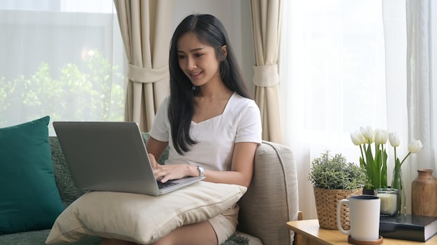 Mulher milenar feliz relaxando no sofá e usando computador portátil