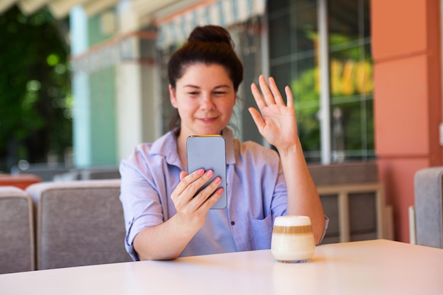 Mulher milenar sorridente do lado de fora com smartphone acenou com a mão