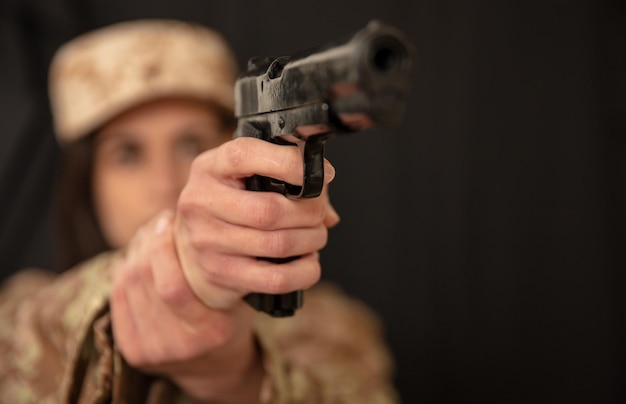 Mulher militar com uma arma na mão apontando para a câmera Soldado feminino em uniforme do exército