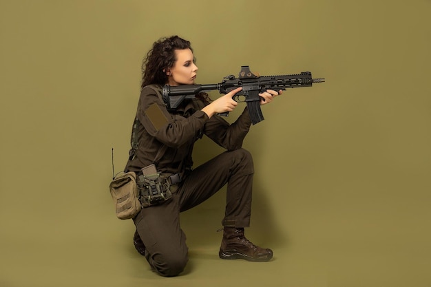 Mulher militar de uniforme verde com colete descarregando com metralhadora nas mãos