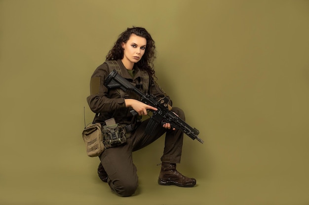 Mulher militar de uniforme verde com colete descarregando com metralhadora nas mãos