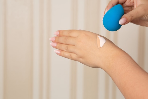 Mulher misturando dois tons de bases líquidas com o liquidificador de beleza azul para encontrar o tom perfeito. Espaço para texto