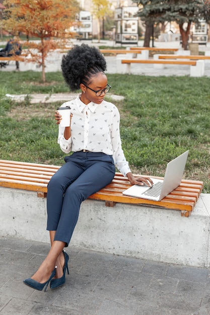 Foto mulher moderna, segurando uma xícara de café enquanto olha para seu laptop