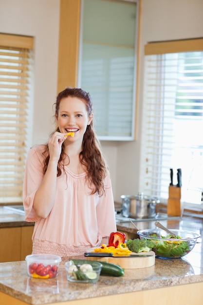 Mulher mordiscando pimentão enquanto preparava salada saudável