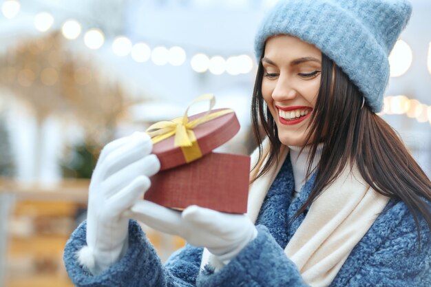 Mulher morena alegre com casaco de inverno, segurando uma caixa de presente na feira de natal. espaço para texto