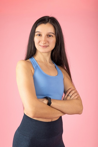 Mulher morena atraente em roupas esportivas da moda em fundo rosa conceito de estilo de vida saudável rosto feliz sorrindo com braços cruzados, olhando para a câmera pessoa positiva