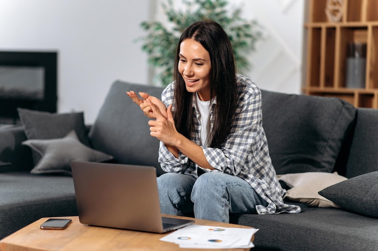 Foto mulher morena bem sucedida caucasiana positiva freelancer ou pequena empresa sentada em um sofá na sala de estar usando um laptop para trabalhar em casa se comunicar com o colega por sorrisos de videochamada