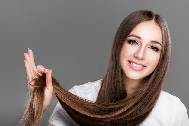 Mulher morena bonita sorridente com cabelo comprido reto brilhante. Cuidado do cabelo