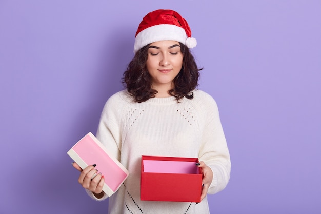 Mulher morena com chapéu de Papai Noel com caixa de presente aberta nas mãos