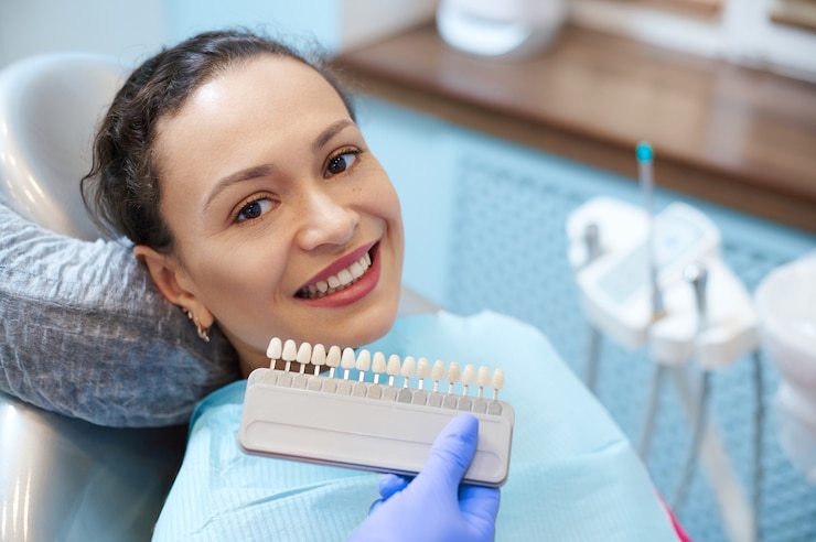 Foto mulher morena com um lindo sorriso antes de receber atendimento odontológico check-up e clareamento de dentes clareamento, médica usando luvas de exame verifica a cor dos dentes com um gráfico de escala de folheado de comparação.