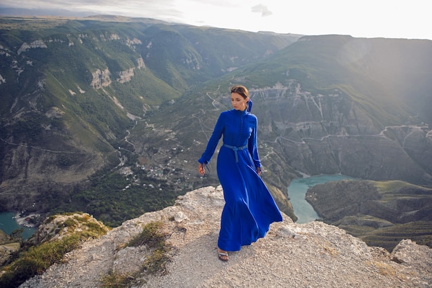 Mulher morena com um vestido longo azul em pé à beira do desfiladeiro Sulak à noite ao pôr do sol no Daguestão