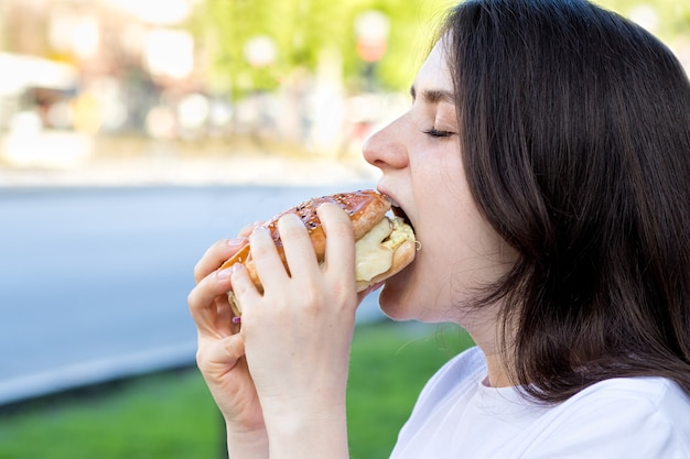 Mulher morena comendo hambúrguer na rua