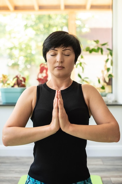 Mulher morena de meia-idade fazendo meditação de ioga em tapete de exercício em casa saúde mental mulher pacífica meditar equilíbrio mental tempo para si mesma alívio do estresse mediação conceito de plenitude da mente