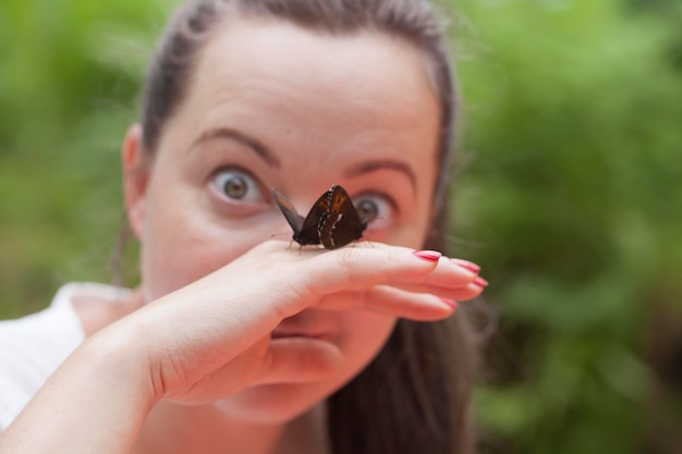Mulher morena de meia-idade olhando surpresa com borboleta na mão ao ar livre