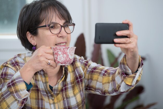 Mulher morena de meia idade usando o smartphone em casa