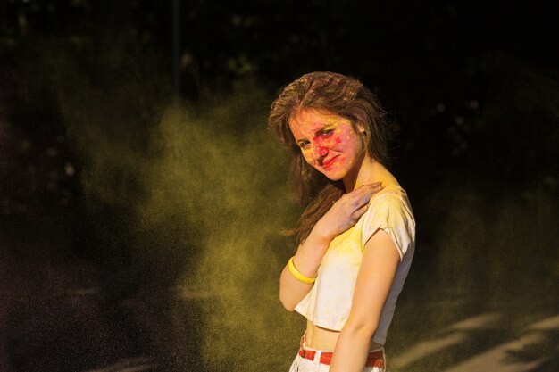 Mulher morena descolada posando em uma nuvem de tinta amarela seca Holi no parque