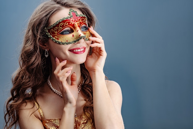 Foto mulher morena em uma máscara de carnaval colorido sobre um fundo azul, sorrindo e olhando para cima