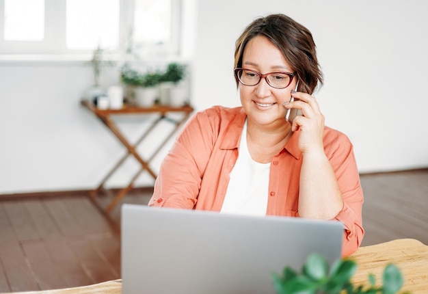 Mulher morena encantadora adulta em óculos plus size corpo positivo trabalhando com laptop em casa