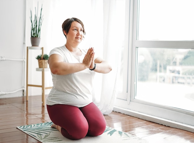 Mulher morena encantadora adulta plus size corpo positivo prática ioga no estúdio brilhante