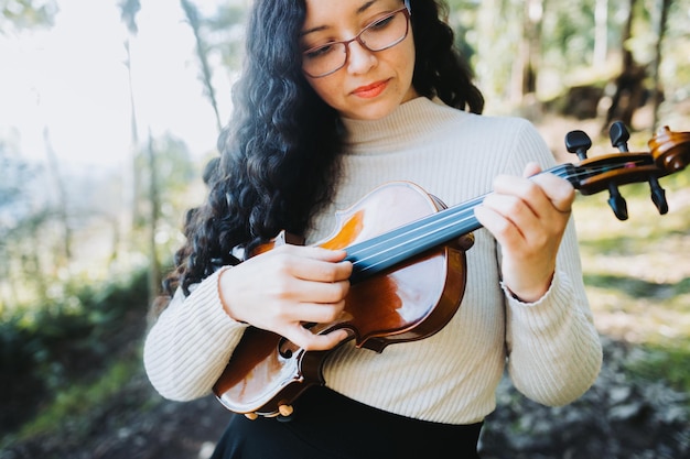 mulher morena encaracolada usando óculos e fazendo técnica de pizzicato em violino Foco seletivo