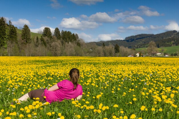 Mulher morena encontra-se em um campo de dente de leão amarelo.