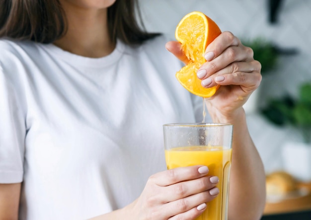 Mulher morena espreme suco de laranja no copo na cozinha leve