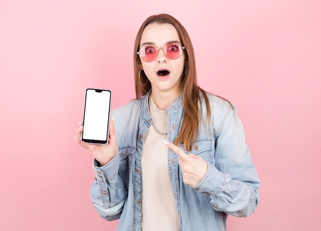 Mulher morena feliz surpresa com jaqueta jeans mostrando a tela do smartphone em branco