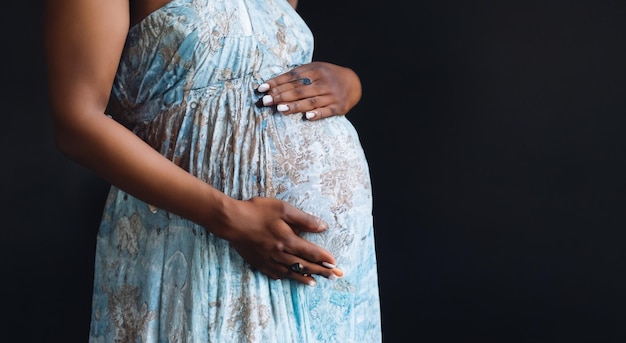 Mulher morena grávida tocando sua barriga em vestido longo em fundo cinza em alta resolução e nitidez