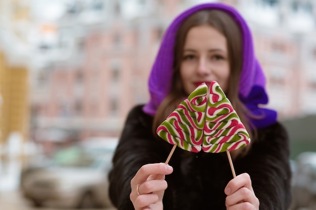 Mulher morena incrível vestindo roupa de inverno, segurando saborosos doces de caramelo. fundo desfocado