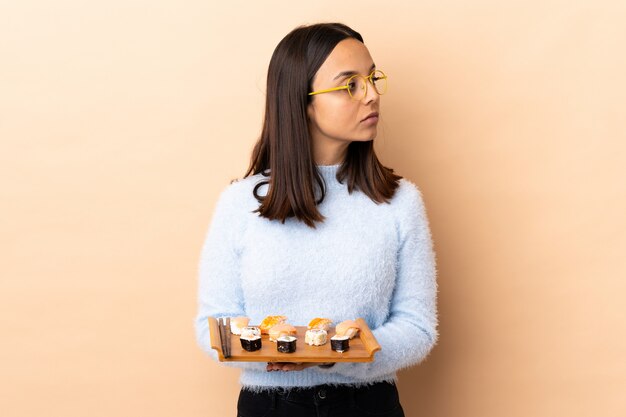 Mulher morena jovem de raça mista, segurando o sushi isolado mantendo os braços cruzados