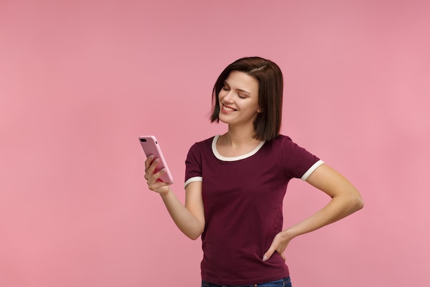 Mulher morena jovem engraçada segurando smartphone rosa e sorrindo.