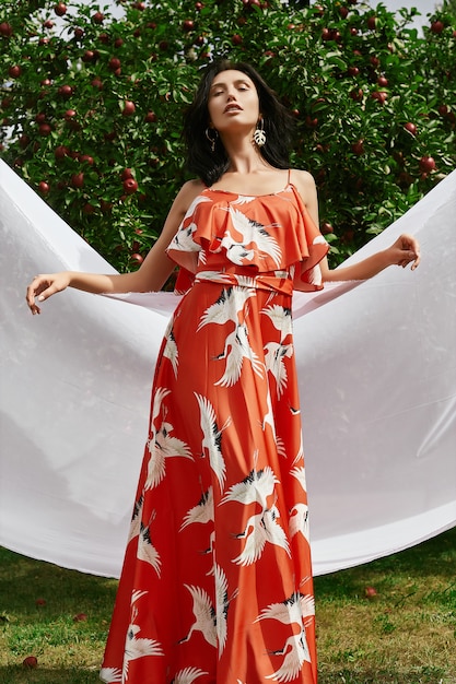 Mulher morena linda no vestido da moda laranja no jardim de maçã