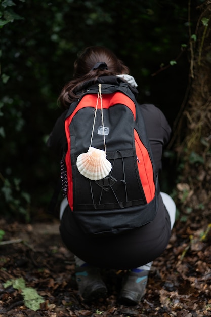 Mulher morena peregrina fazendo o Caminho de Santiago agachada olhando para uma caverna cheia de plantas