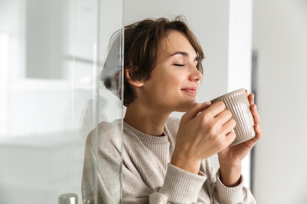 Mulher morena satisfeita tomando café com os olhos fechados e goza em casa