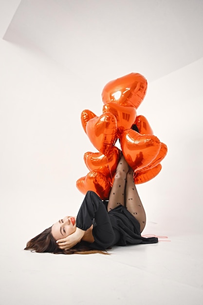 Mulher morena segurando um monte de balões vermelhos em forma de coração no estúdio