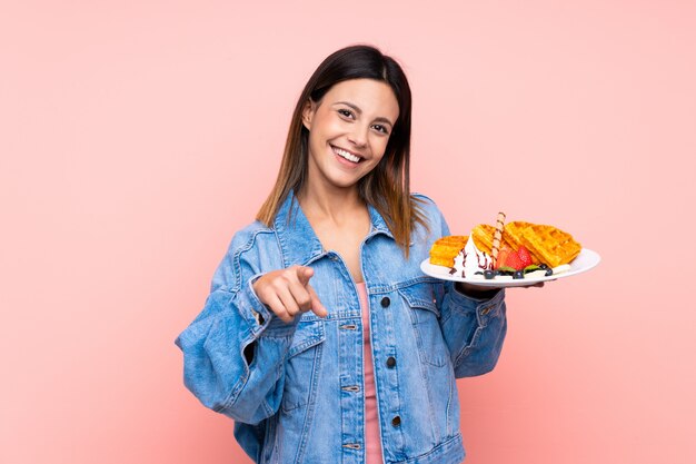 Mulher morena segurando waffles aponta o dedo para você com uma expressão confiante